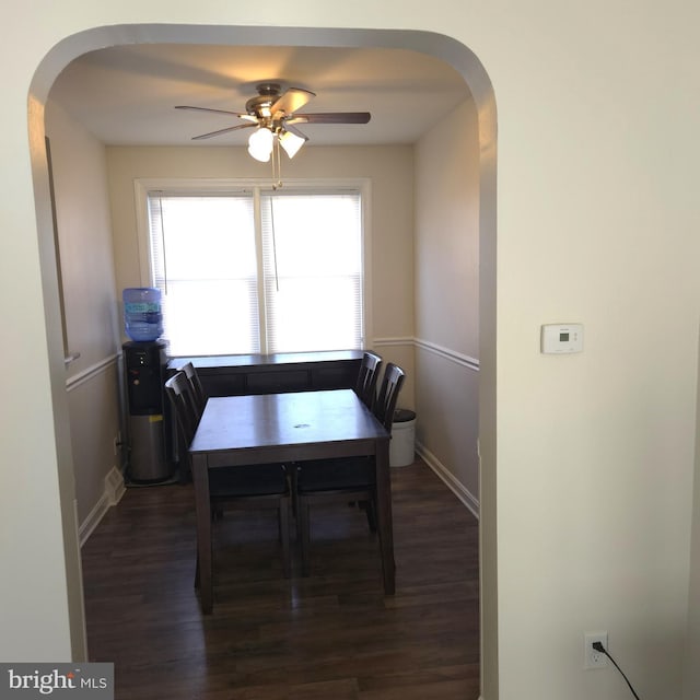 dining space featuring dark wood-style floors, arched walkways, ceiling fan, and baseboards