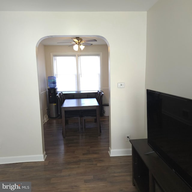 dining room with ceiling fan, baseboards, dark wood finished floors, and arched walkways