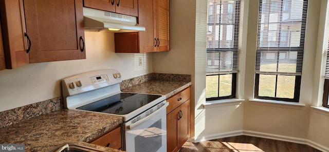 kitchen with white electric stove, baseboards, brown cabinetry, dark wood-style flooring, and under cabinet range hood