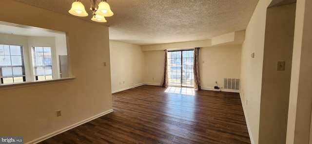 unfurnished room featuring a textured ceiling, a notable chandelier, dark wood-style flooring, visible vents, and baseboards