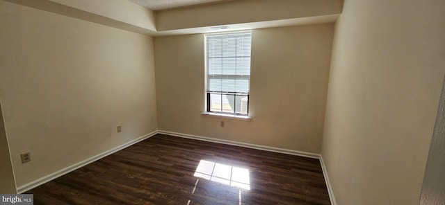 spare room with dark wood-type flooring, visible vents, and baseboards