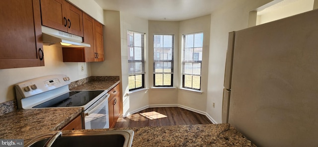 kitchen featuring dark wood finished floors, brown cabinetry, freestanding refrigerator, white electric range, and under cabinet range hood