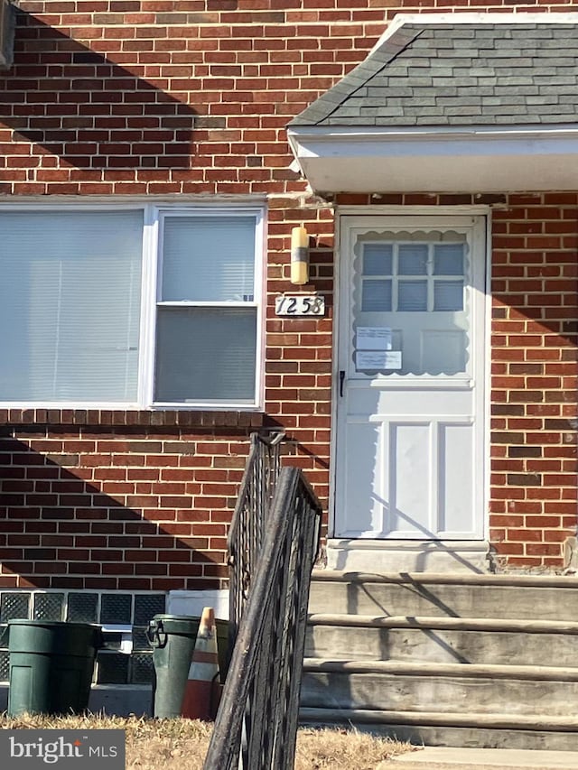 property entrance featuring brick siding and a shingled roof