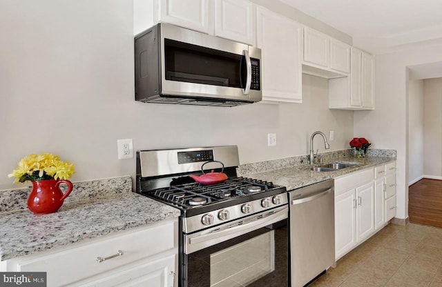 kitchen featuring light stone counters, light tile patterned floors, stainless steel appliances, white cabinetry, and a sink