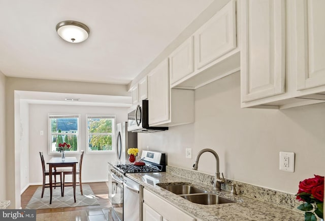 kitchen featuring baseboards, white cabinets, light stone countertops, stainless steel appliances, and a sink