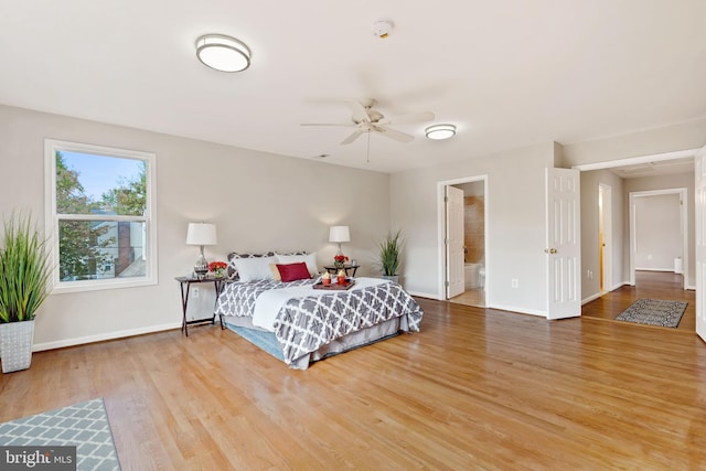 bedroom with ensuite bathroom, wood finished floors, and baseboards