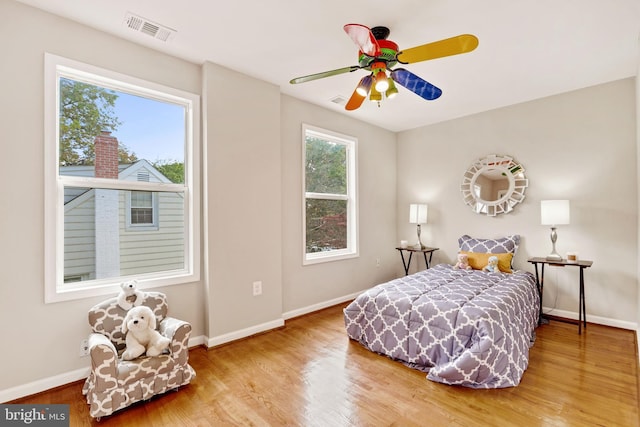 bedroom with baseboards, multiple windows, visible vents, and wood finished floors