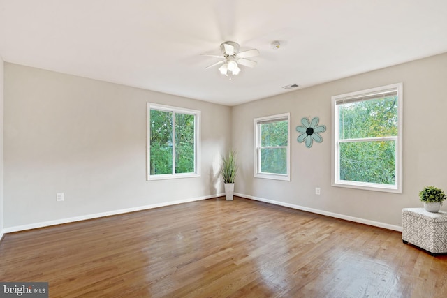 spare room with a ceiling fan, visible vents, baseboards, and wood finished floors