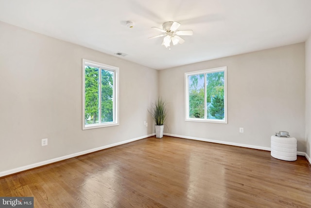 unfurnished room featuring a wealth of natural light, visible vents, baseboards, and wood finished floors