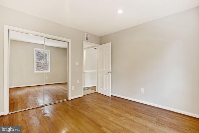 unfurnished bedroom with a closet, wood-type flooring, visible vents, and baseboards