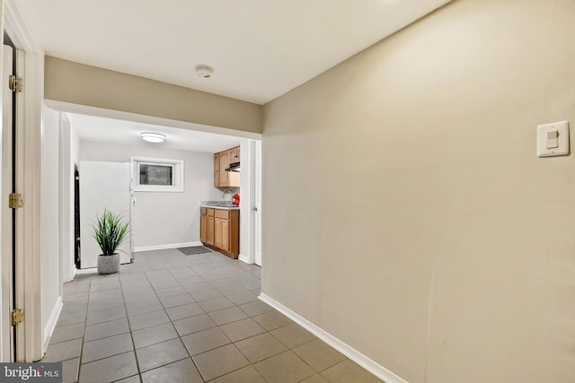 hall featuring light tile patterned floors, a sink, and baseboards