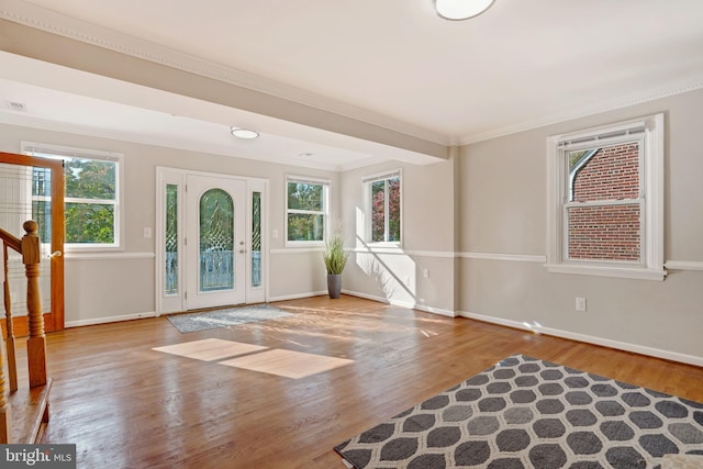 foyer featuring baseboards, light wood-type flooring, a wealth of natural light, and crown molding