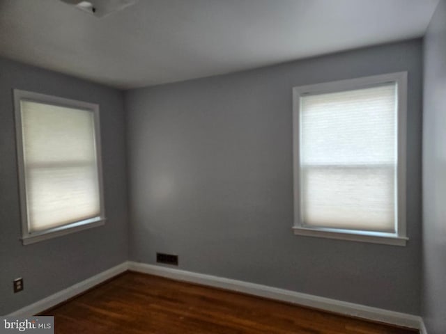 empty room with dark wood-style floors, visible vents, and baseboards