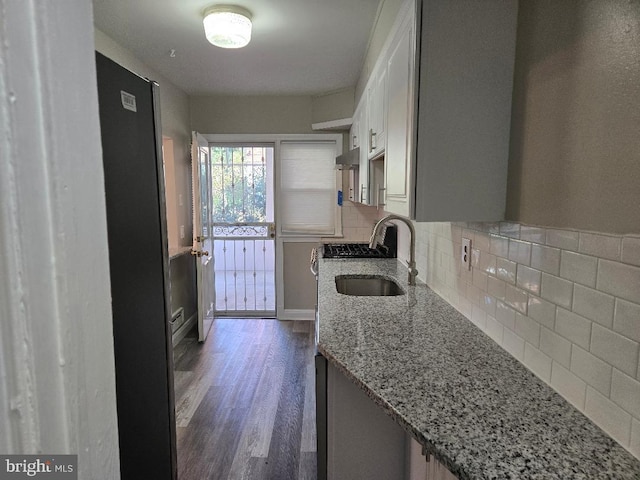 kitchen with light stone counters, under cabinet range hood, a sink, decorative backsplash, and dark wood finished floors