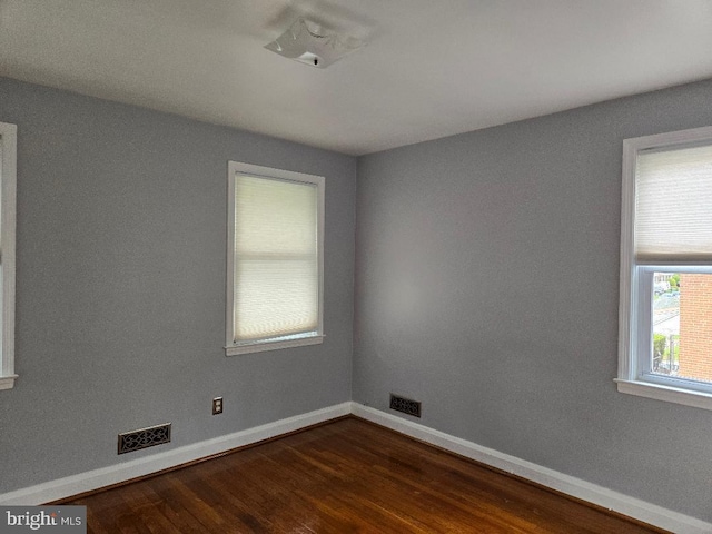 unfurnished room featuring dark wood finished floors, visible vents, and baseboards