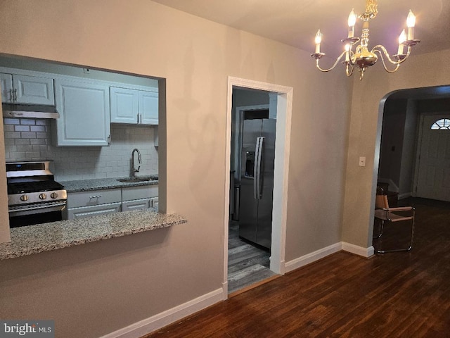 kitchen featuring light stone counters, decorative light fixtures, stainless steel appliances, under cabinet range hood, and a sink