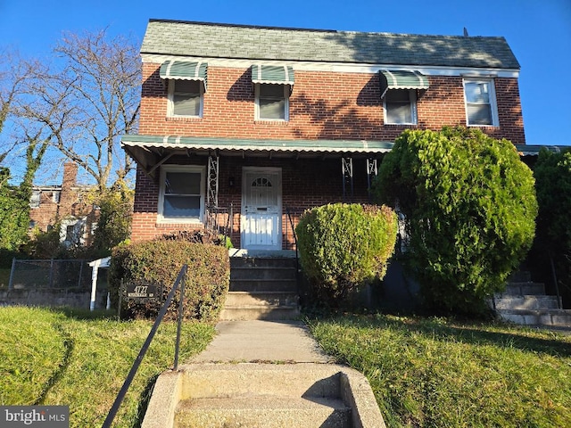 view of front of property featuring roof with shingles, a front lawn, and brick siding