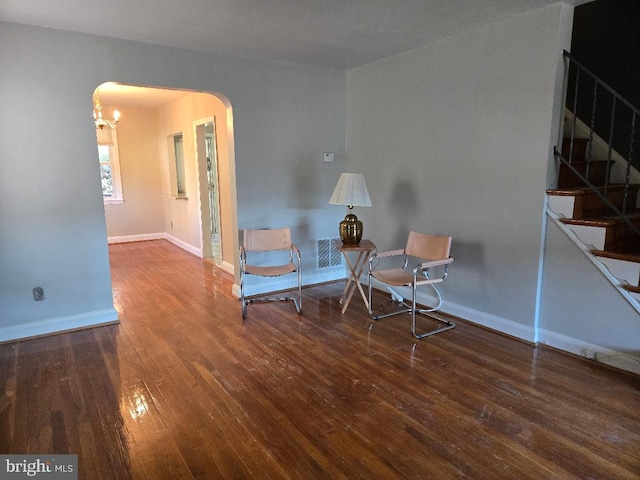 living area with arched walkways, stairway, baseboards, and wood finished floors