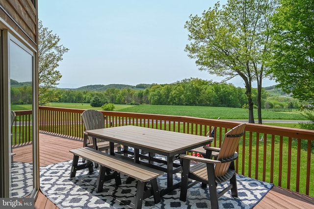 deck with a forest view, outdoor dining area, and a lawn