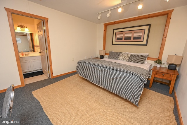 carpeted bedroom featuring track lighting, a sink, ensuite bath, and baseboards