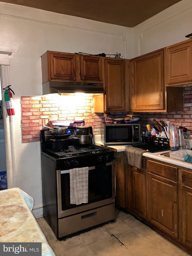 kitchen featuring appliances with stainless steel finishes, brown cabinets, under cabinet range hood, and decorative backsplash