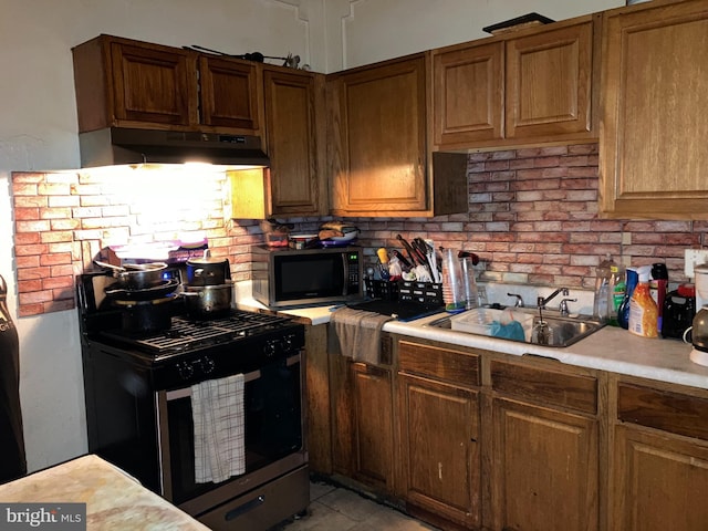 kitchen featuring under cabinet range hood, a sink, light countertops, brown cabinetry, and stainless steel range with gas stovetop