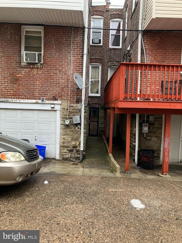 rear view of property featuring an attached garage, stone siding, cooling unit, and brick siding