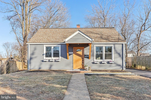 bungalow-style house featuring a front yard, a chimney, fence, and roof with shingles