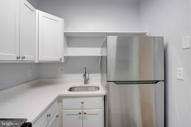 kitchen featuring white cabinets, freestanding refrigerator, light countertops, open shelves, and a sink