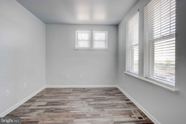 unfurnished room with visible vents, plenty of natural light, baseboards, and wood finished floors