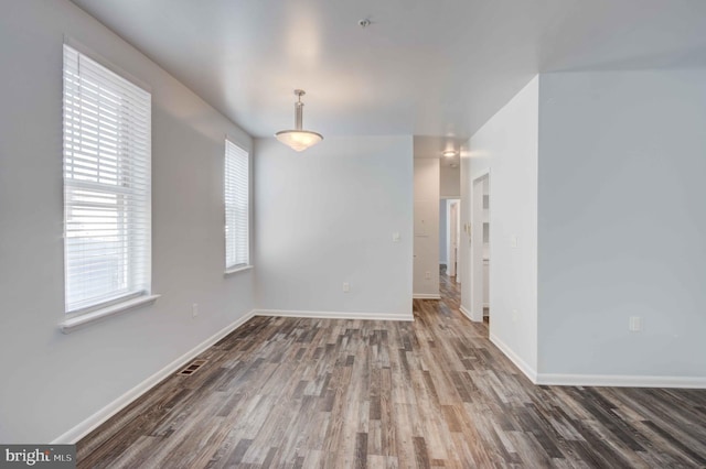 empty room with dark wood-style floors, visible vents, and baseboards