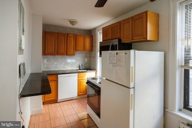 kitchen featuring brown cabinets, dark countertops, white appliances, and light tile patterned flooring