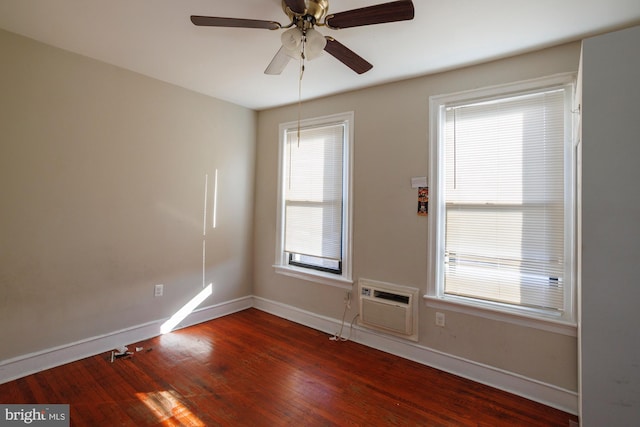 spare room featuring dark wood-style flooring, a wall unit AC, a ceiling fan, and baseboards