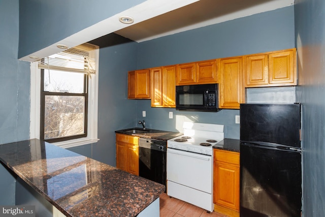 kitchen featuring brown cabinetry, dark stone counters, a sink, and black appliances