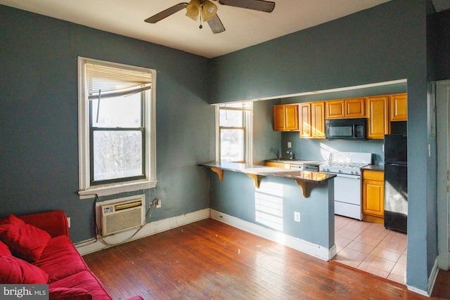 kitchen featuring brown cabinetry, a peninsula, black appliances, a kitchen bar, and a wall mounted AC