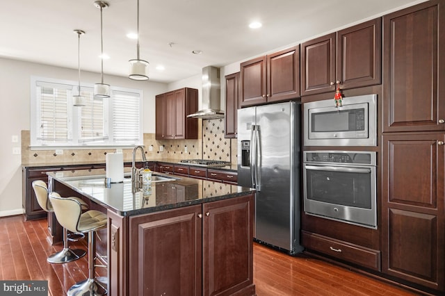 kitchen featuring dark wood-style flooring, stainless steel appliances, tasteful backsplash, a sink, and wall chimney exhaust hood