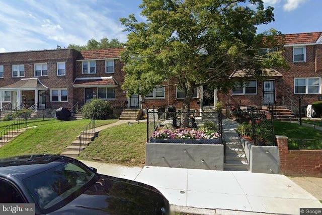 multi unit property with brick siding, a front yard, and fence