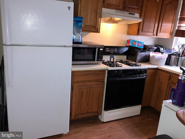 kitchen featuring under cabinet range hood, light countertops, freestanding refrigerator, stainless steel microwave, and gas stove