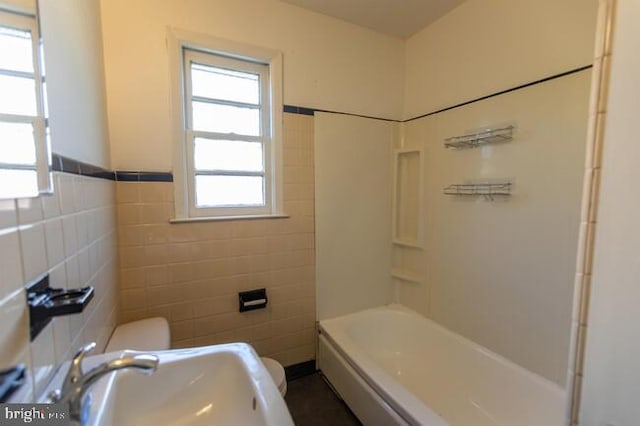 bathroom with toilet, a wainscoted wall, a sink, and tile walls