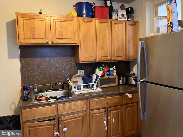 kitchen with dark countertops, decorative backsplash, brown cabinetry, freestanding refrigerator, and a sink