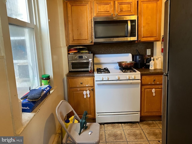 kitchen featuring brown cabinets, dark countertops, stainless steel appliances, and backsplash