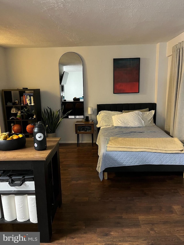 bedroom featuring a textured ceiling, arched walkways, and dark wood-style flooring