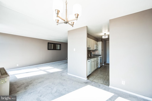 kitchen with an inviting chandelier, white microwave, gas stove, white cabinets, and light carpet