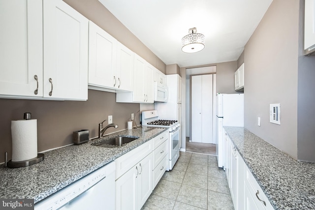 kitchen featuring stone countertops, white appliances, white cabinets, and a sink