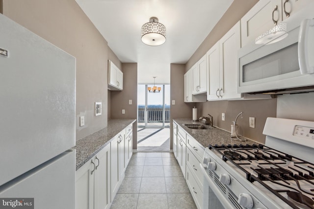 kitchen featuring white appliances, stone countertops, white cabinets, a sink, and a notable chandelier