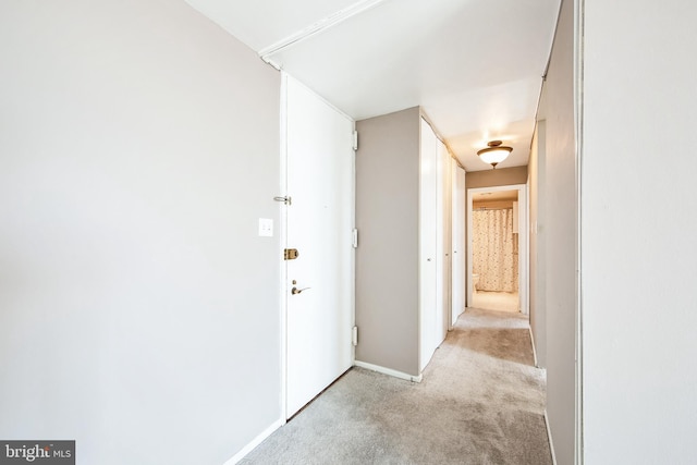 corridor featuring baseboards and light colored carpet