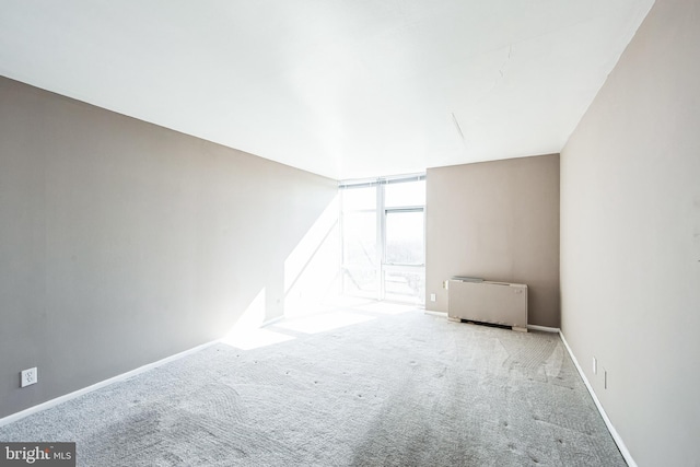 carpeted empty room featuring baseboards and radiator