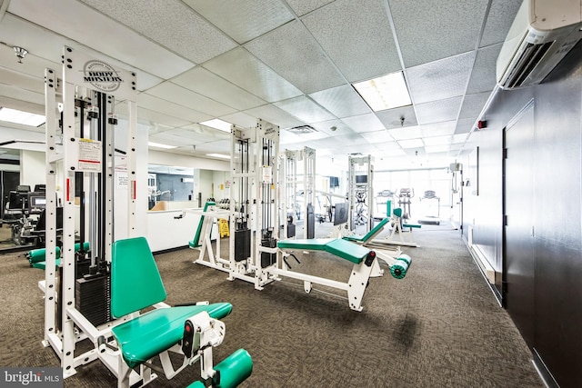 exercise room with a drop ceiling, a wall mounted air conditioner, and visible vents