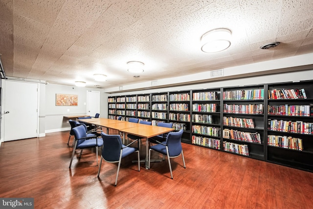 interior space featuring visible vents, a barn door, wall of books, a textured ceiling, and wood finished floors