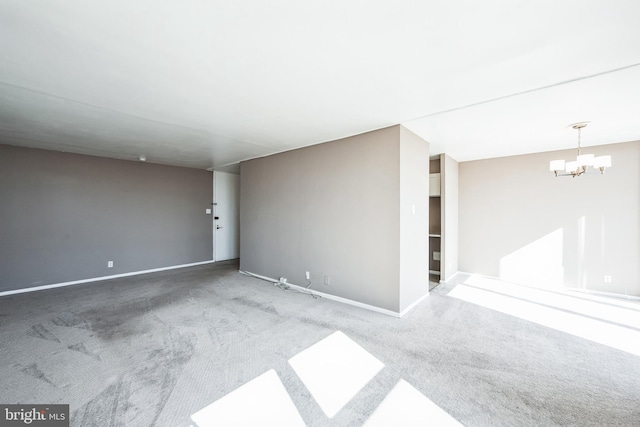 carpeted spare room with a notable chandelier and baseboards